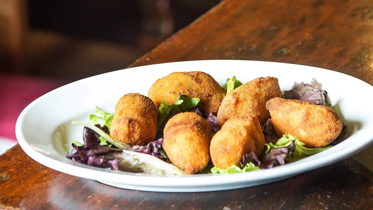 Oval white plate of golden fried croquettes on a bed of mixed salad greens