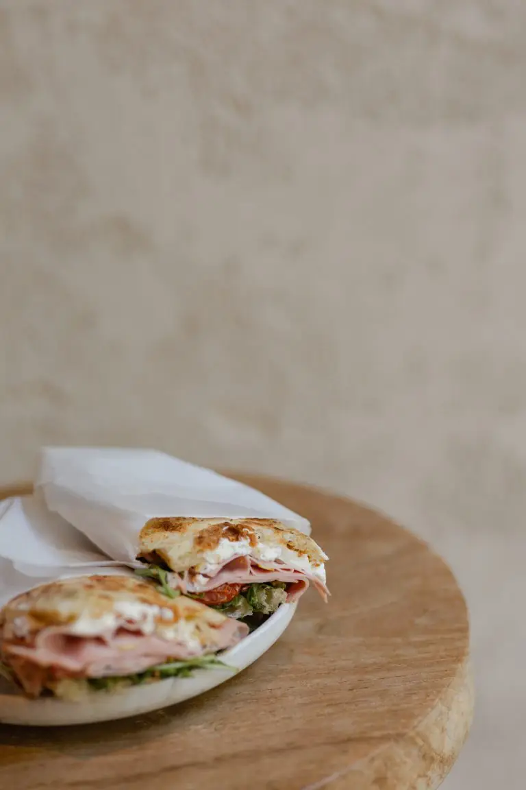 Toasted ham and cheese sandwich cut in half, showing melted cheese, ham, arugula, and tomato, on a plate at Maldita Barra