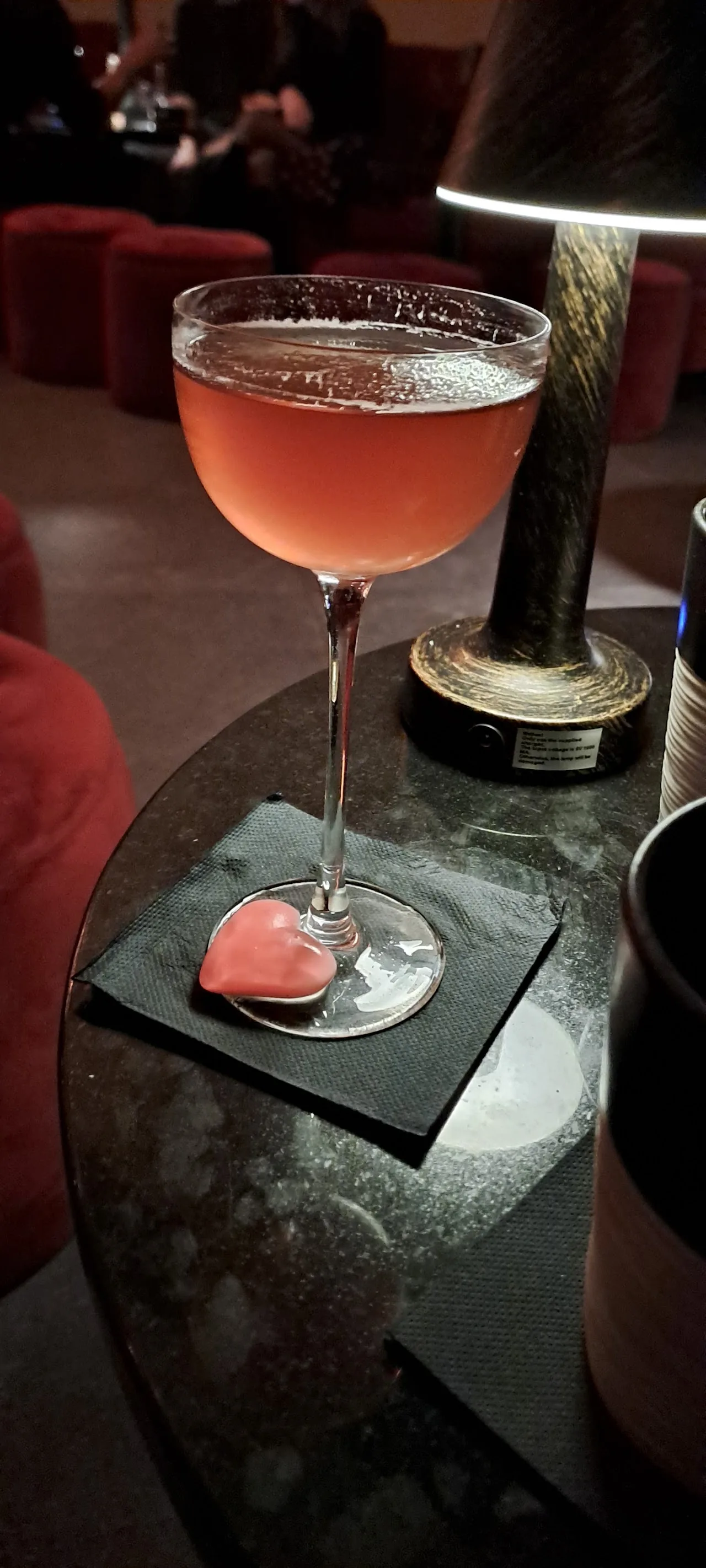A pink cocktail garnished with a slice of fruit on a black table
