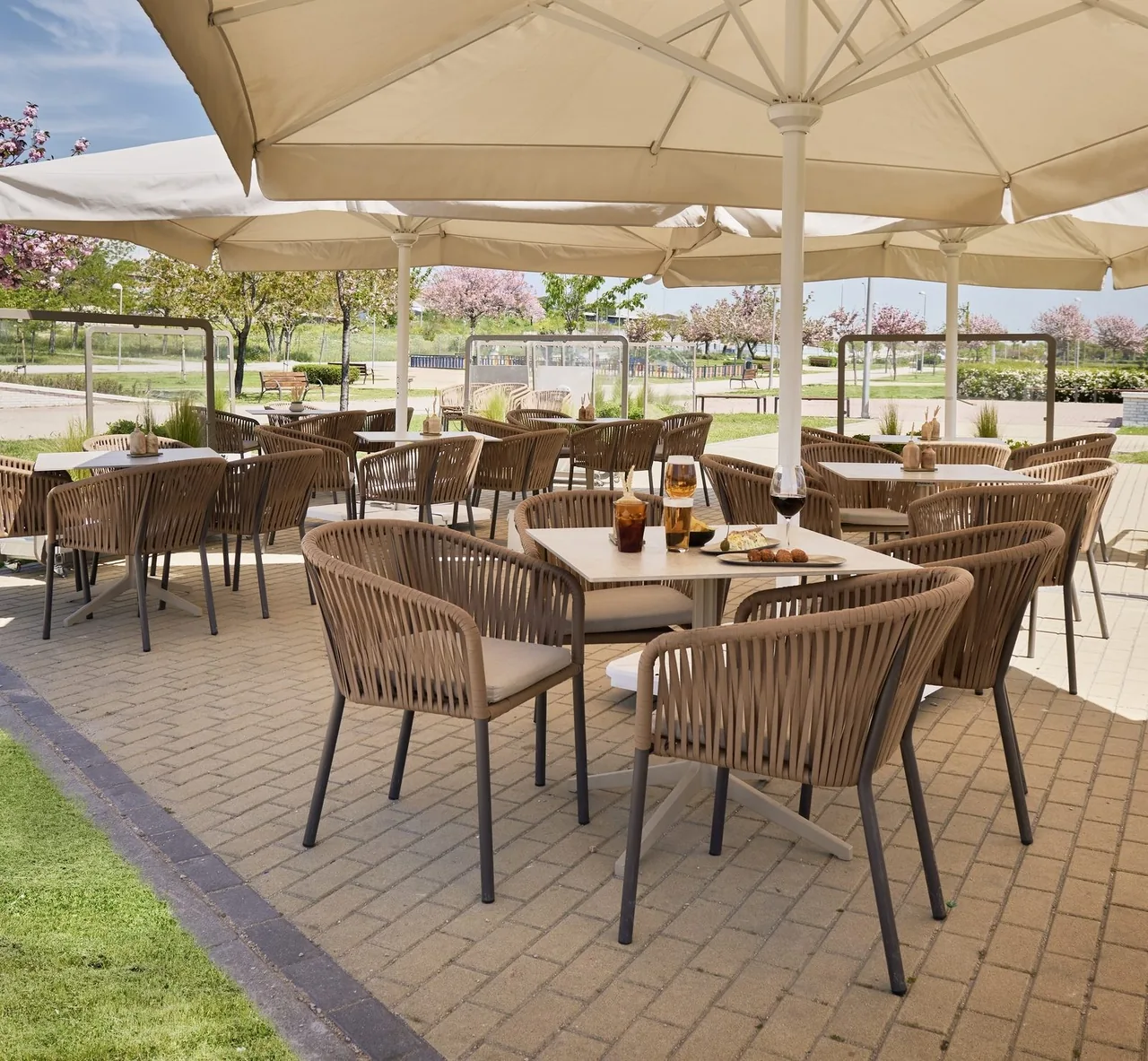A shaded outdoor terrace with wicker chairs and tables under large parasols