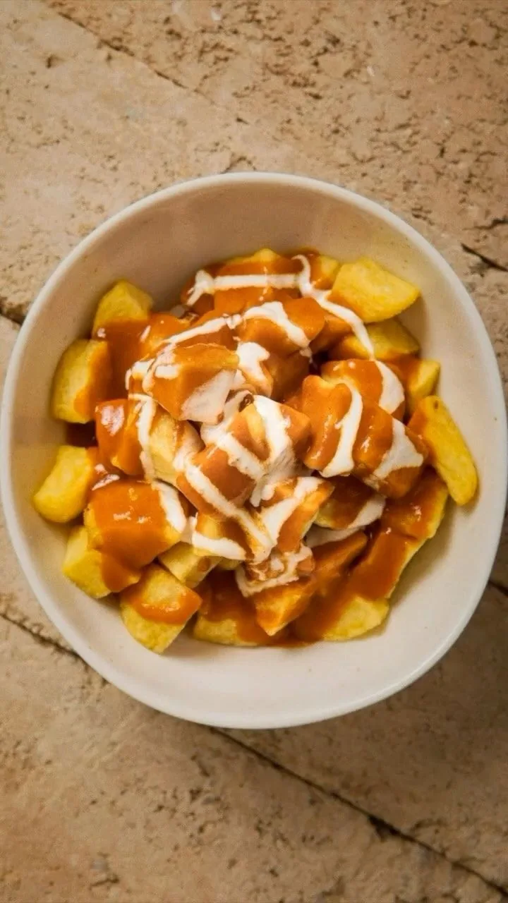 A white bowl of fried potatoes topped with a red sauce and a white drizzle