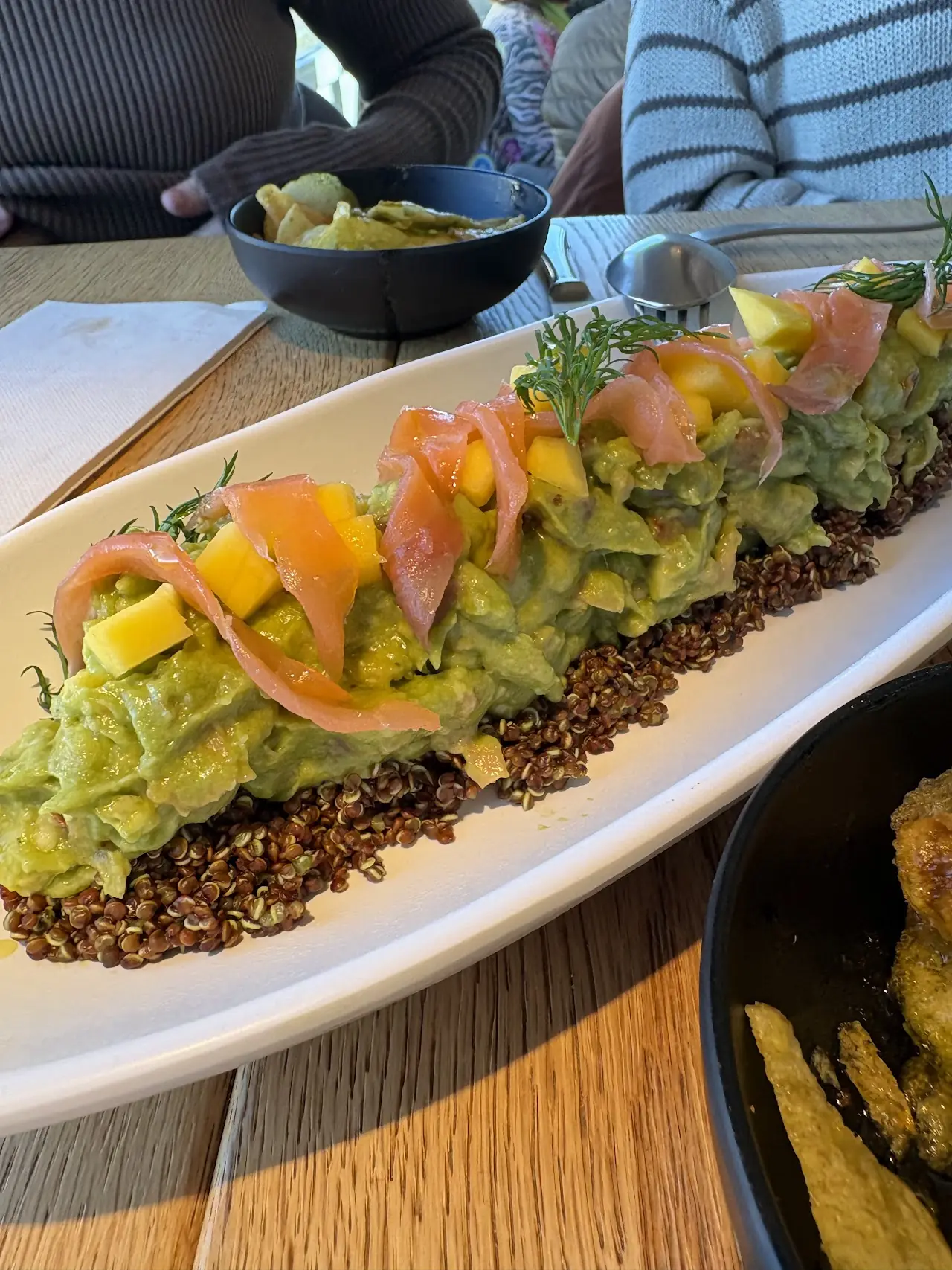 Avocado and quinoa picadillo topped with smoked salmon and mango on a long white plate