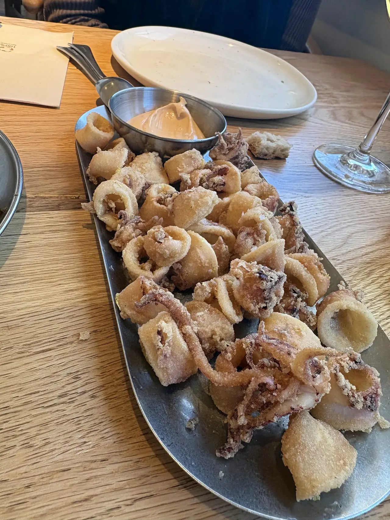 Fried baby squid rings and tentacles on a metal tray with a pot of sauce