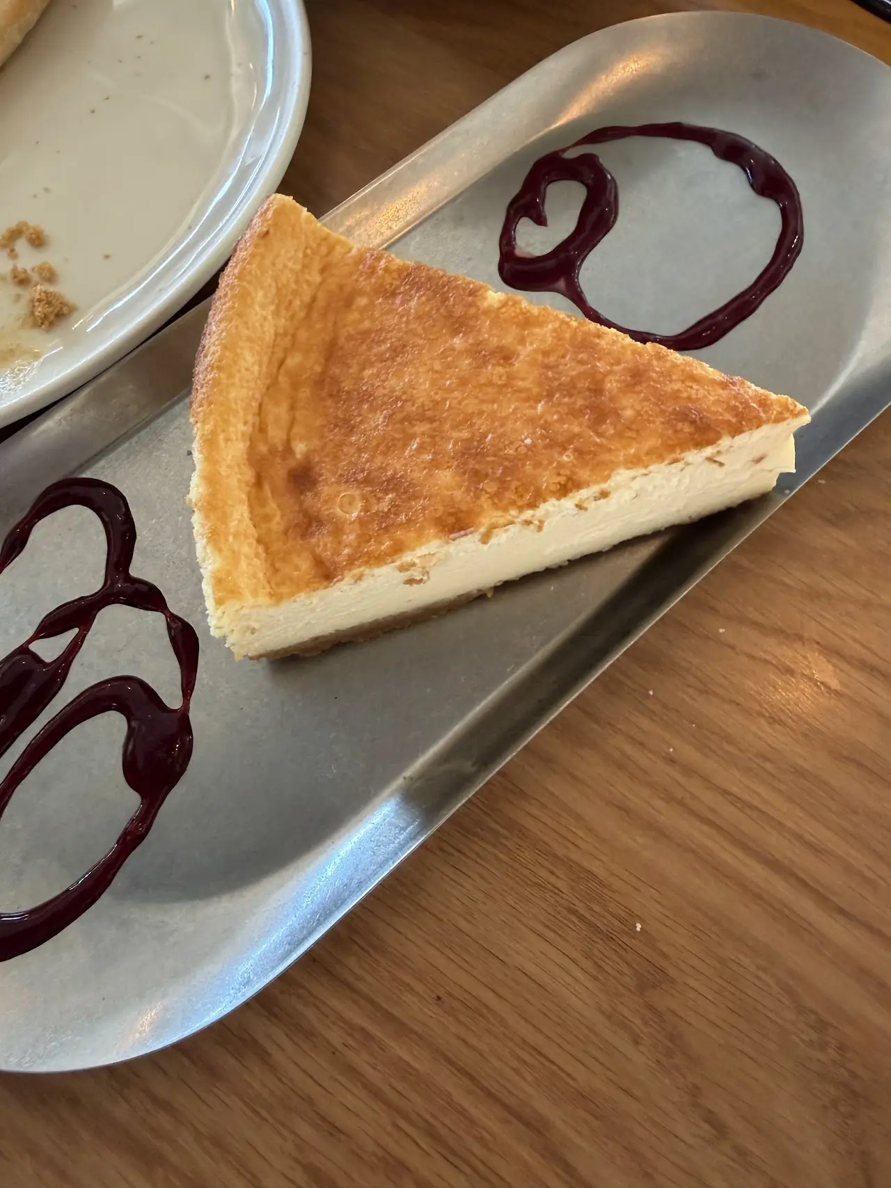 A slice of baked cheesecake with a swirl of berry sauce on a metal tray