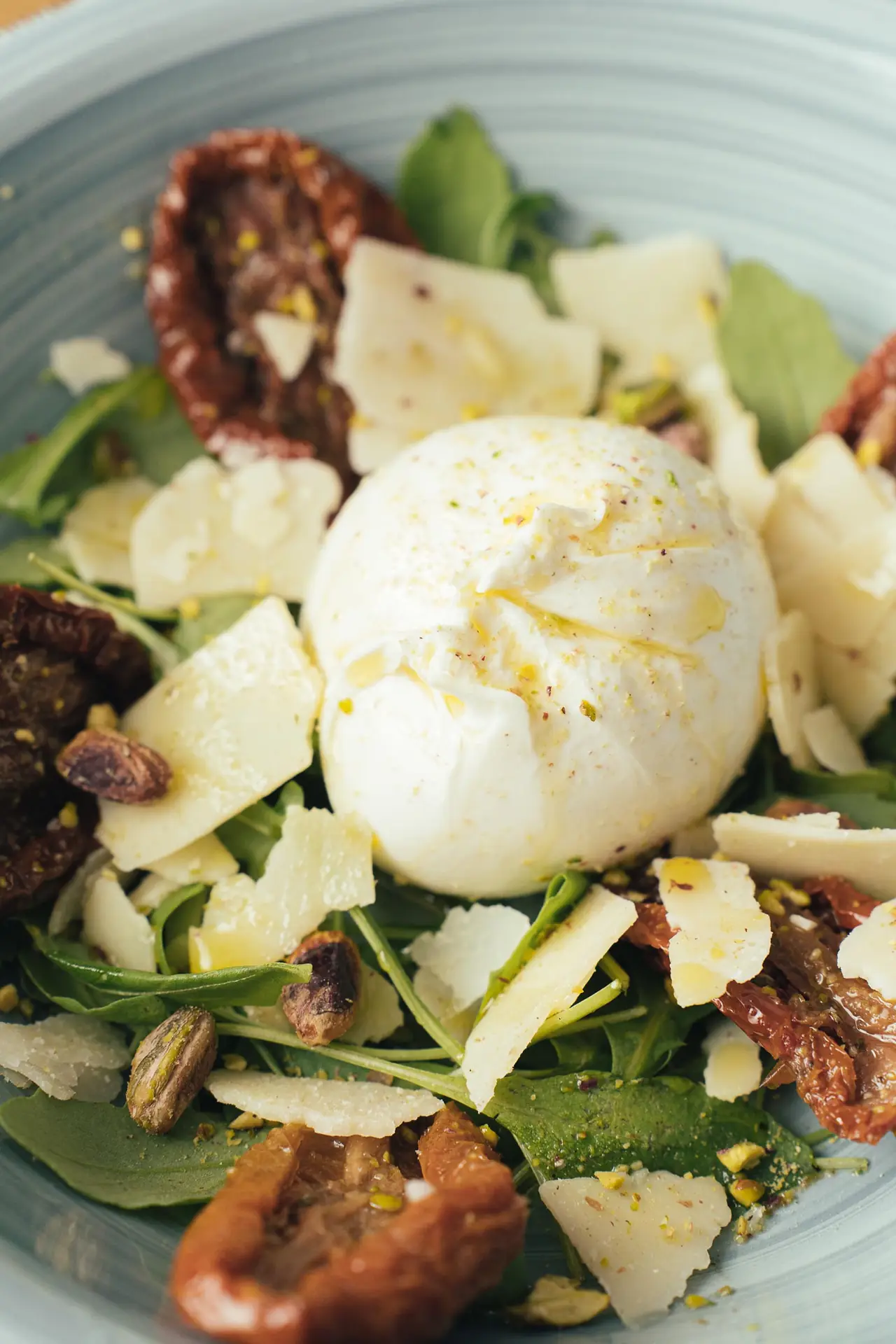 Burrata with shaved parmesan, sun-dried tomatoes, arugula, and pistachios in a bowl at MAMA