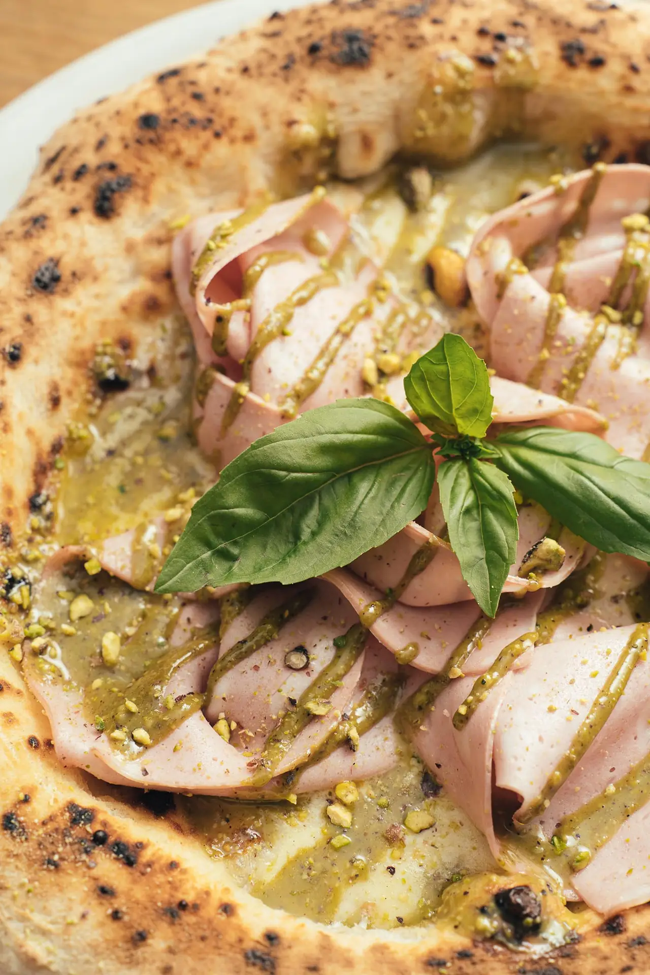 Wood-fired pizza with rolled mortadella, pistachio cream drizzle, crushed pistachios, and fresh basil at MAMA