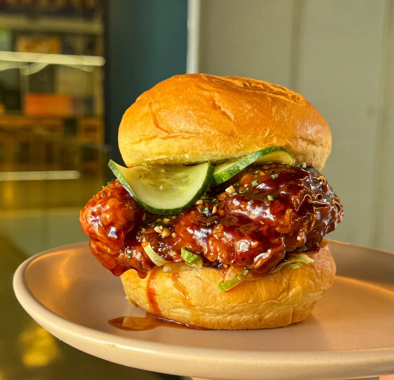 A fried chicken burger with pickles and sriracha glaze on a bun