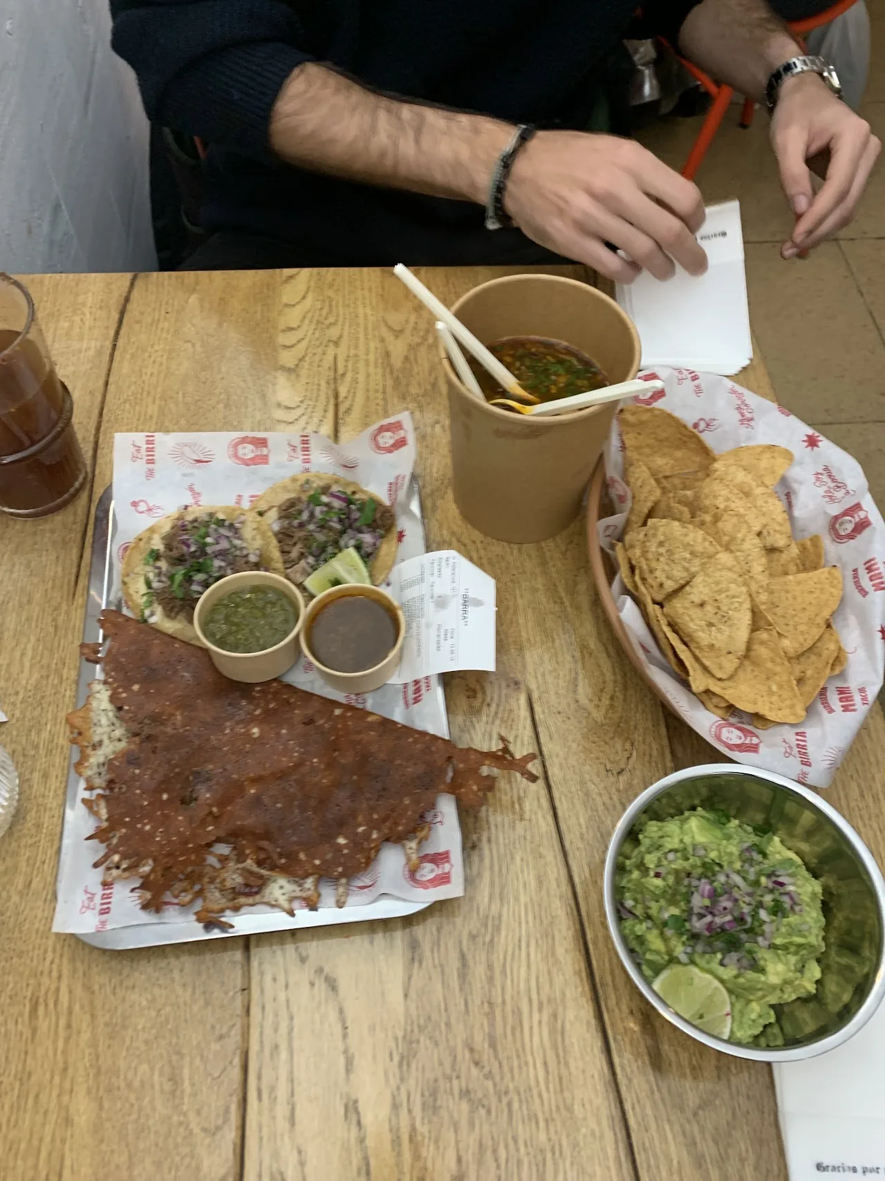A birria taco plate with a cup of consomme and guacamole