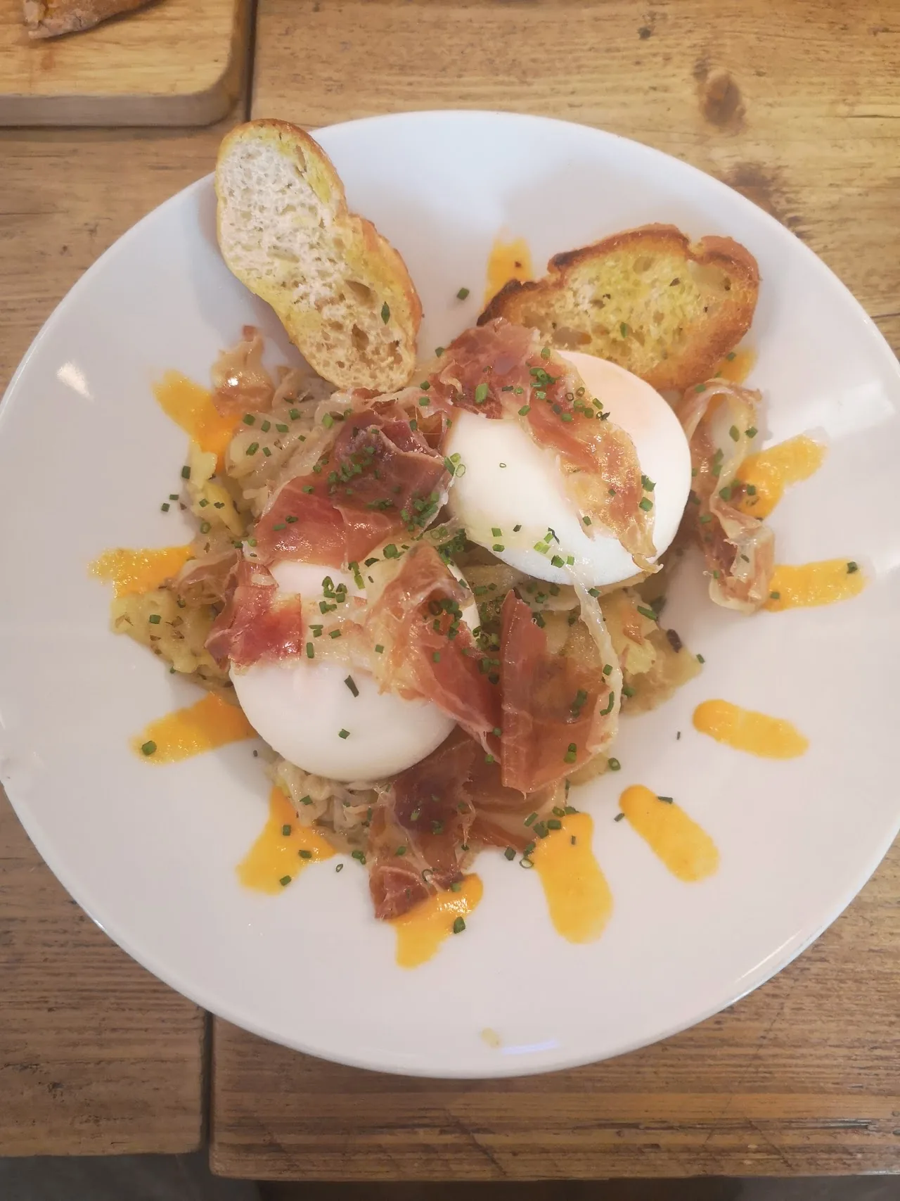 A dish of poached eggs over toast with bacon and greens, drizzled with sauce