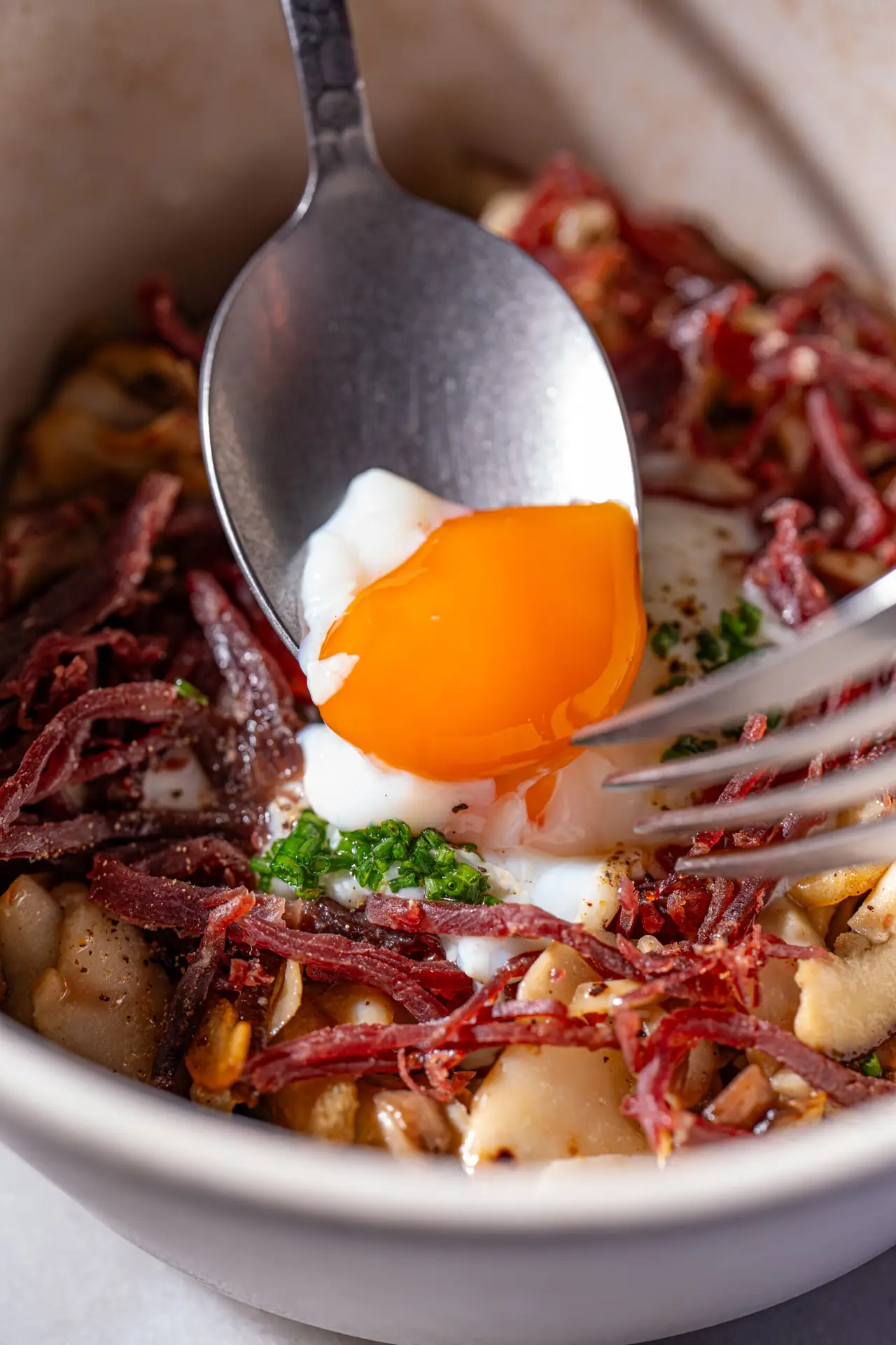 Runny poached egg yolk spooned over crispy jamón, wild mushrooms, and chives in a bowl, Manda Huev0s