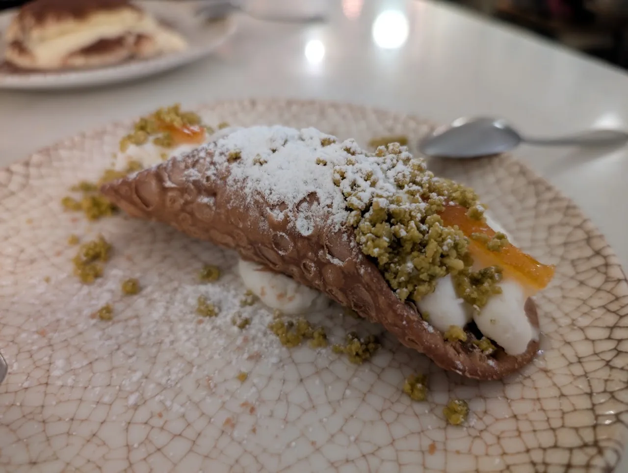 A cannolo pastry dusted with powdered sugar and pistachio