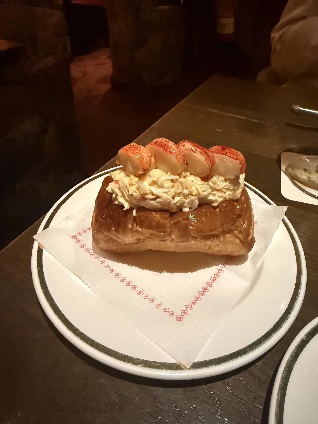 An open brioche roll piled with lobster and seafood on a plate