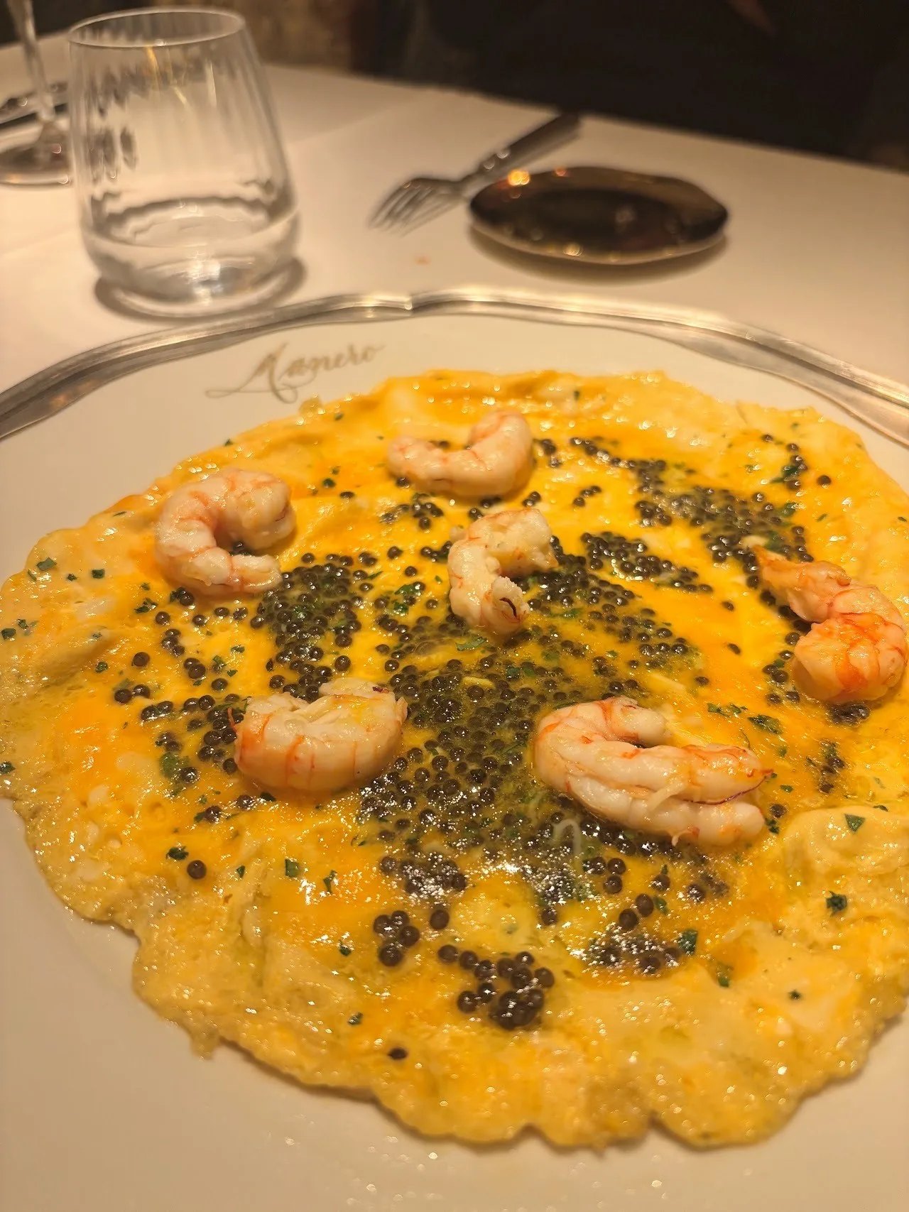 A round plate of scrambled egg topped with prawns and dark caviar