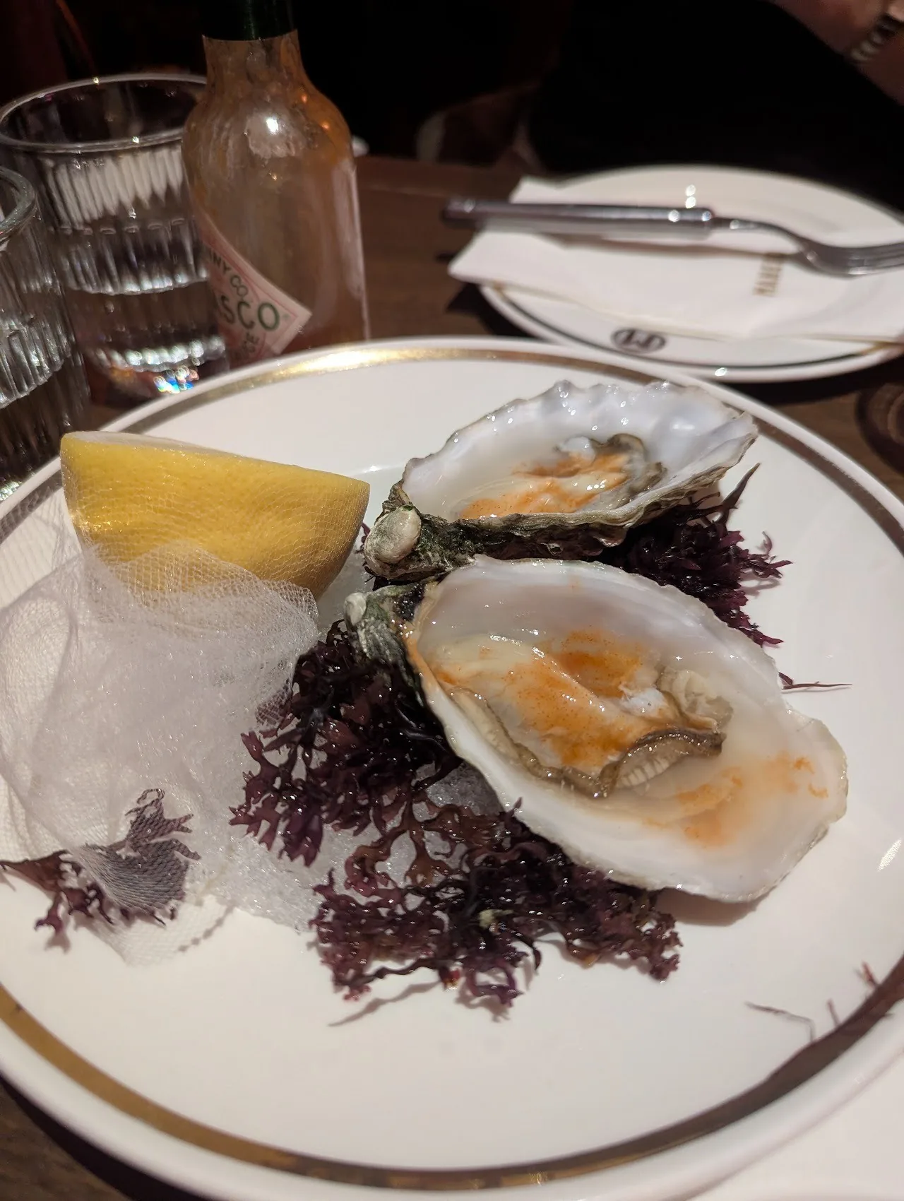 Two oysters on seaweed on a white plate with a lemon wedge