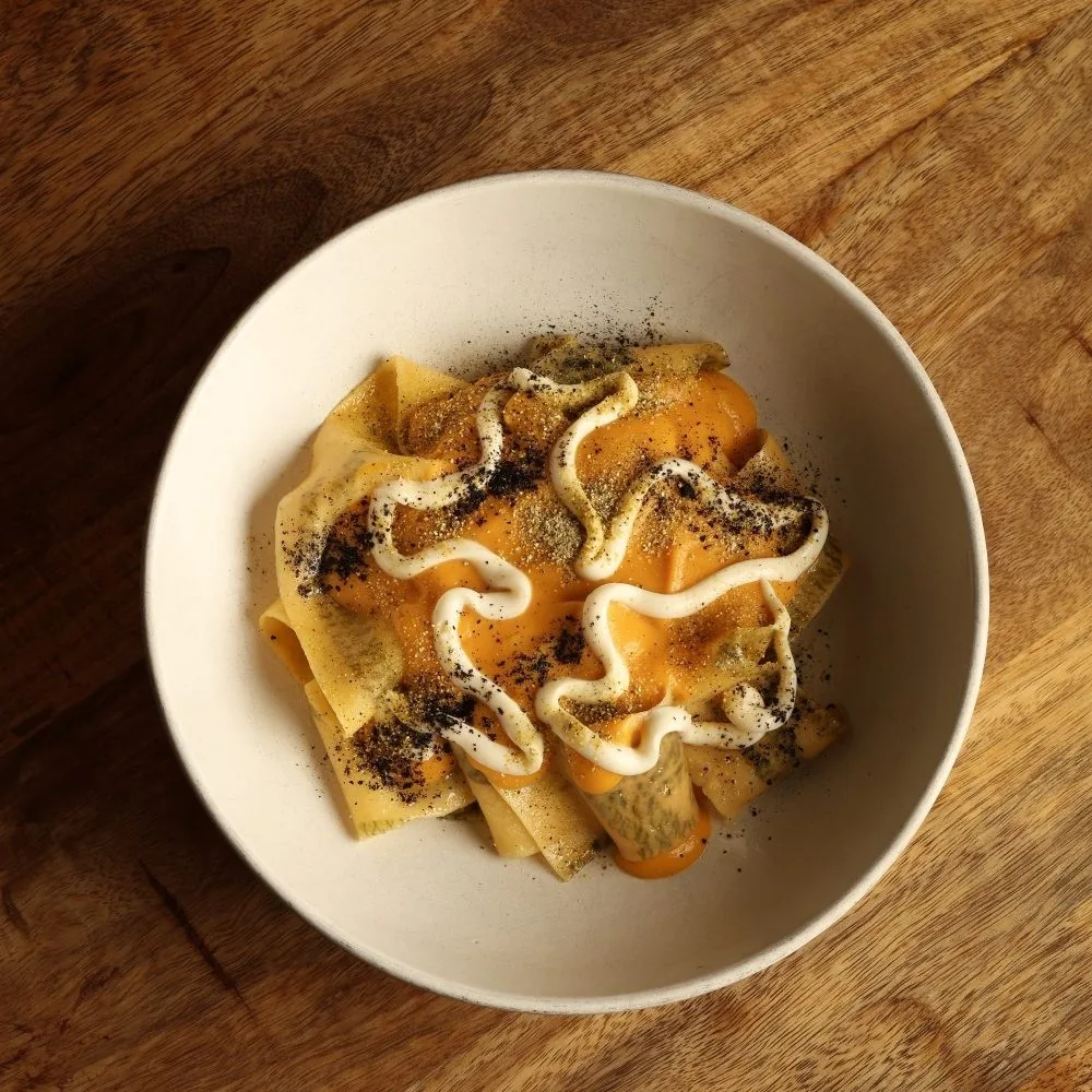 A cream bowl of pasta with orange sauce, white cream and dark seasoning on a wooden table