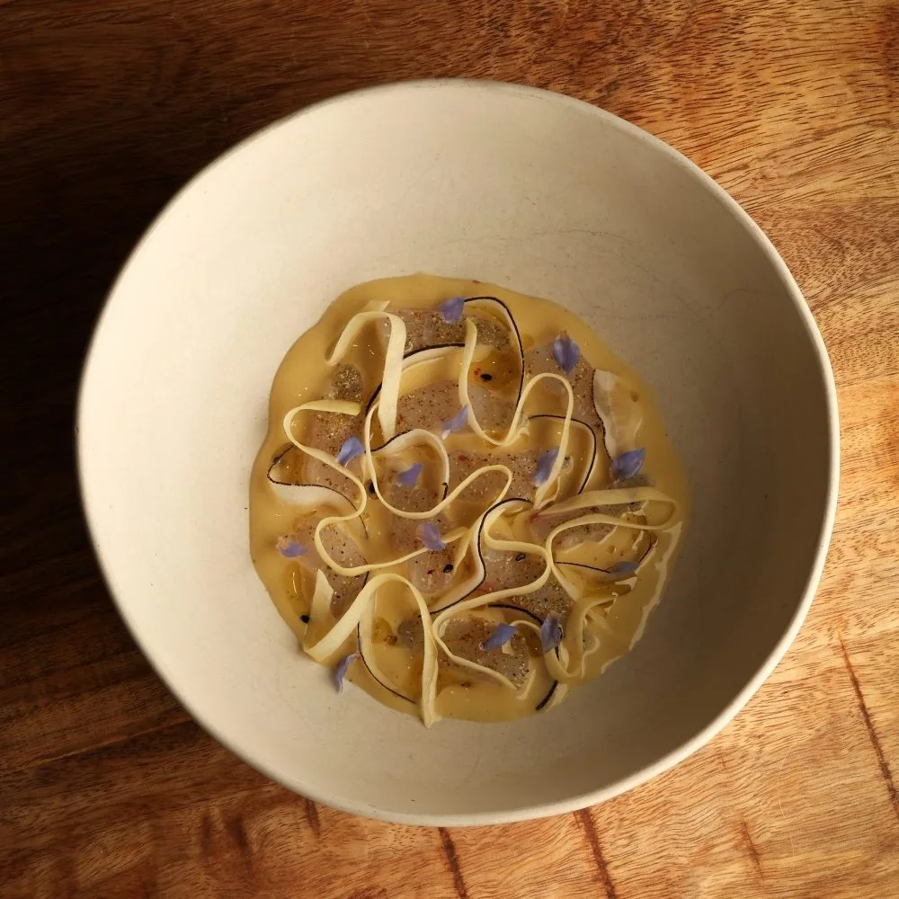 A cream bowl of thin pasta ribbons with small purple flowers