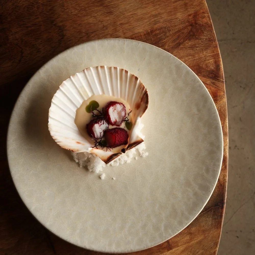 A scallop shell with red garnish on a large cream plate