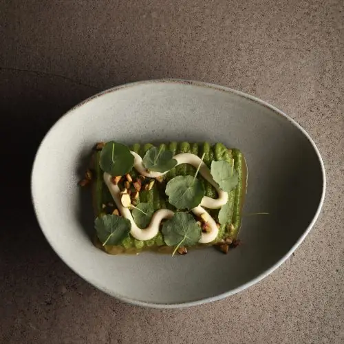 Green vegetable dish topped with nuts, herbs and a cream drizzle in a bowl