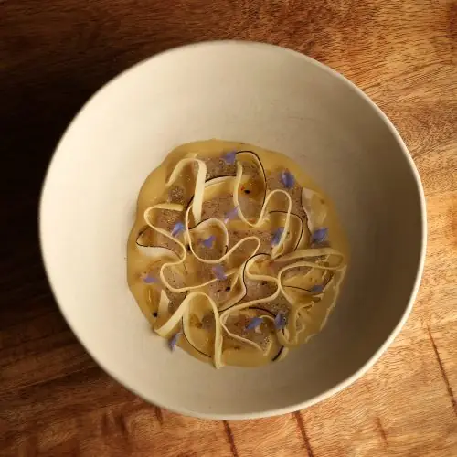 Bowl of pasta ribbons in a golden broth garnished with purple edible flowers