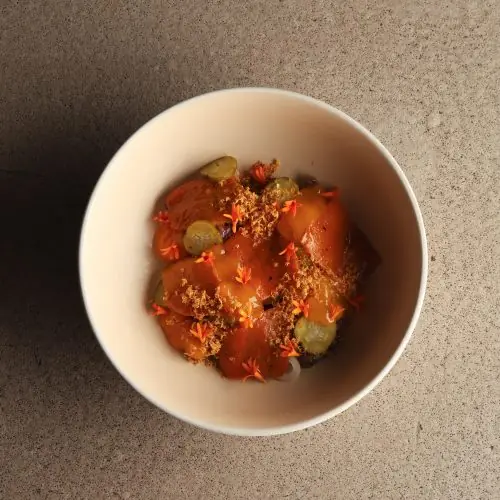 Bowl of tomato and cucumber dish topped with breadcrumbs and orange flowers