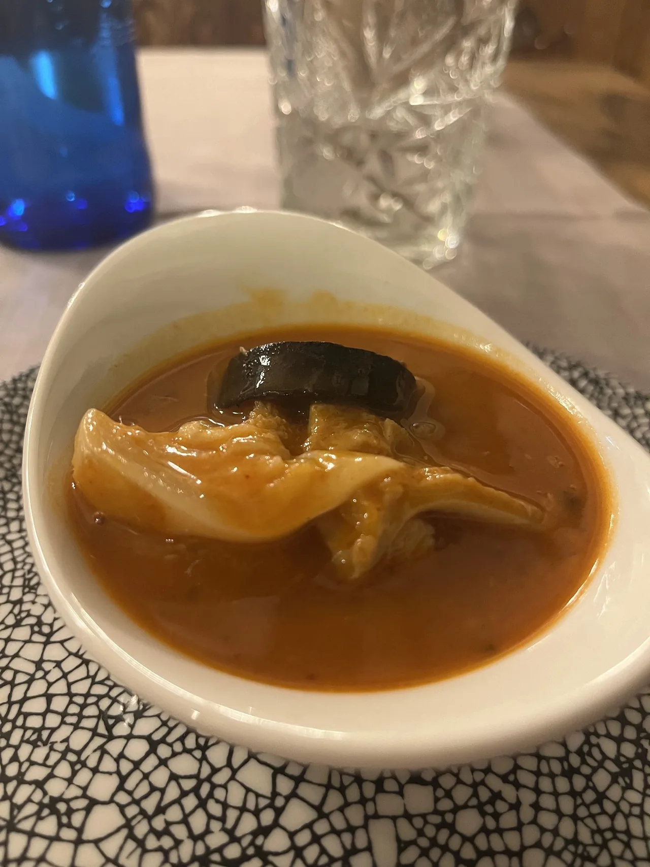 Close view of a white bowl of tripe stew with a slice of black pudding on a patterned plate