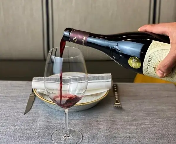 Red wine being poured from a bottle into a stemmed glass at a set table with plate, napkin and cutlery