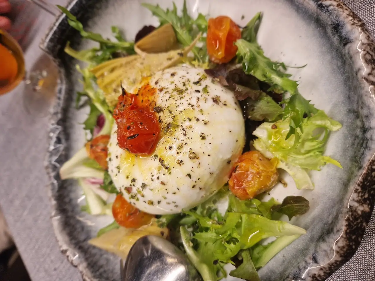 A whole burrata topped with cracked pepper over grilled vegetables and mixed greens.