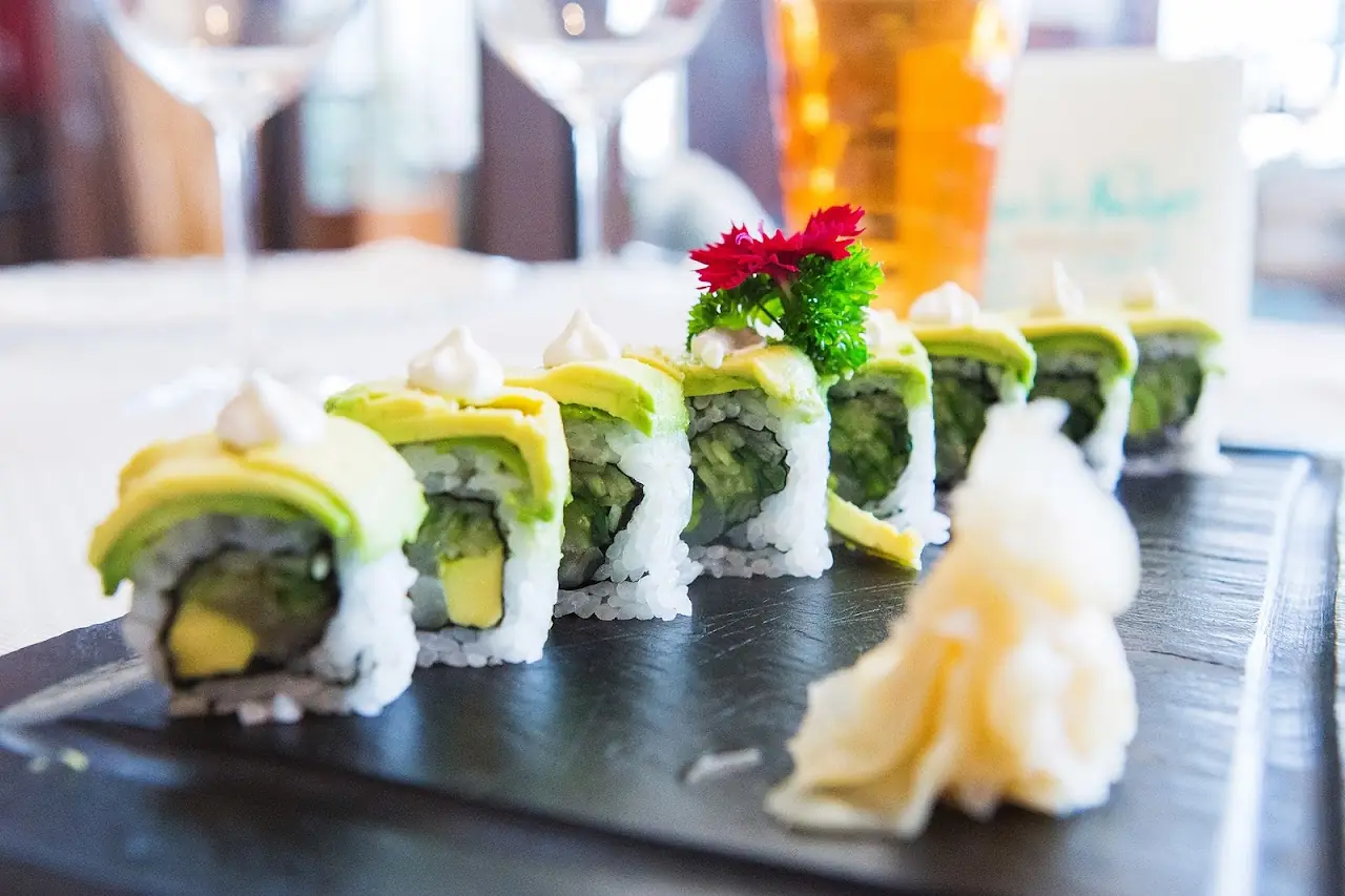 Avocado-wrapped sushi roll sliced and arranged on a black slate with pickled ginger