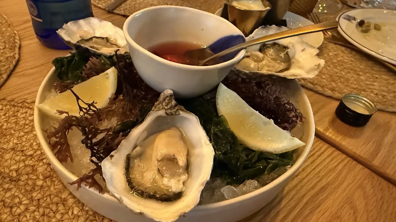 A bowl of oysters on ice with a dipping sauce