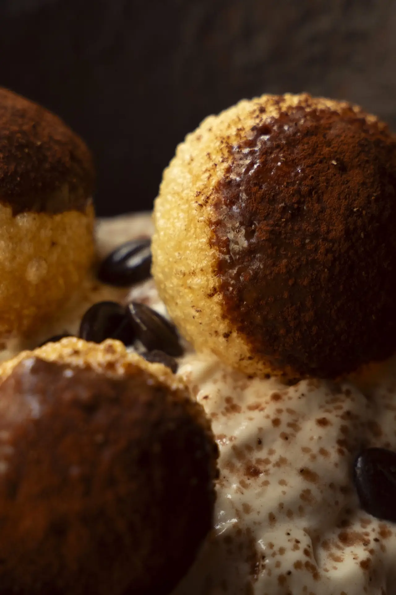 Close-up of cocoa-dusted fried dough balls over a creamy mascarpone base scattered with coffee beans
