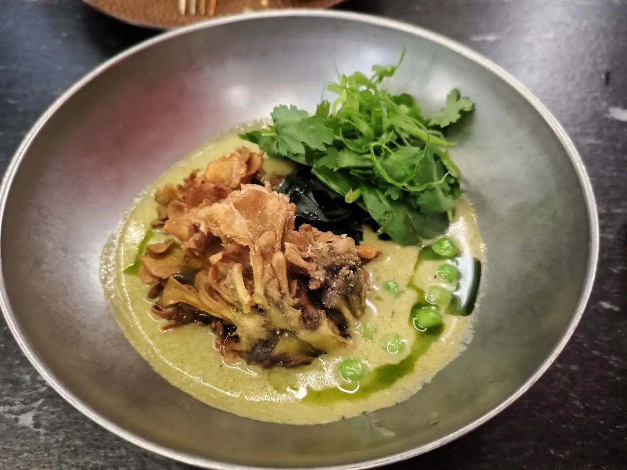 A bowl of braised greens and crispy fried onions in a green herb broth
