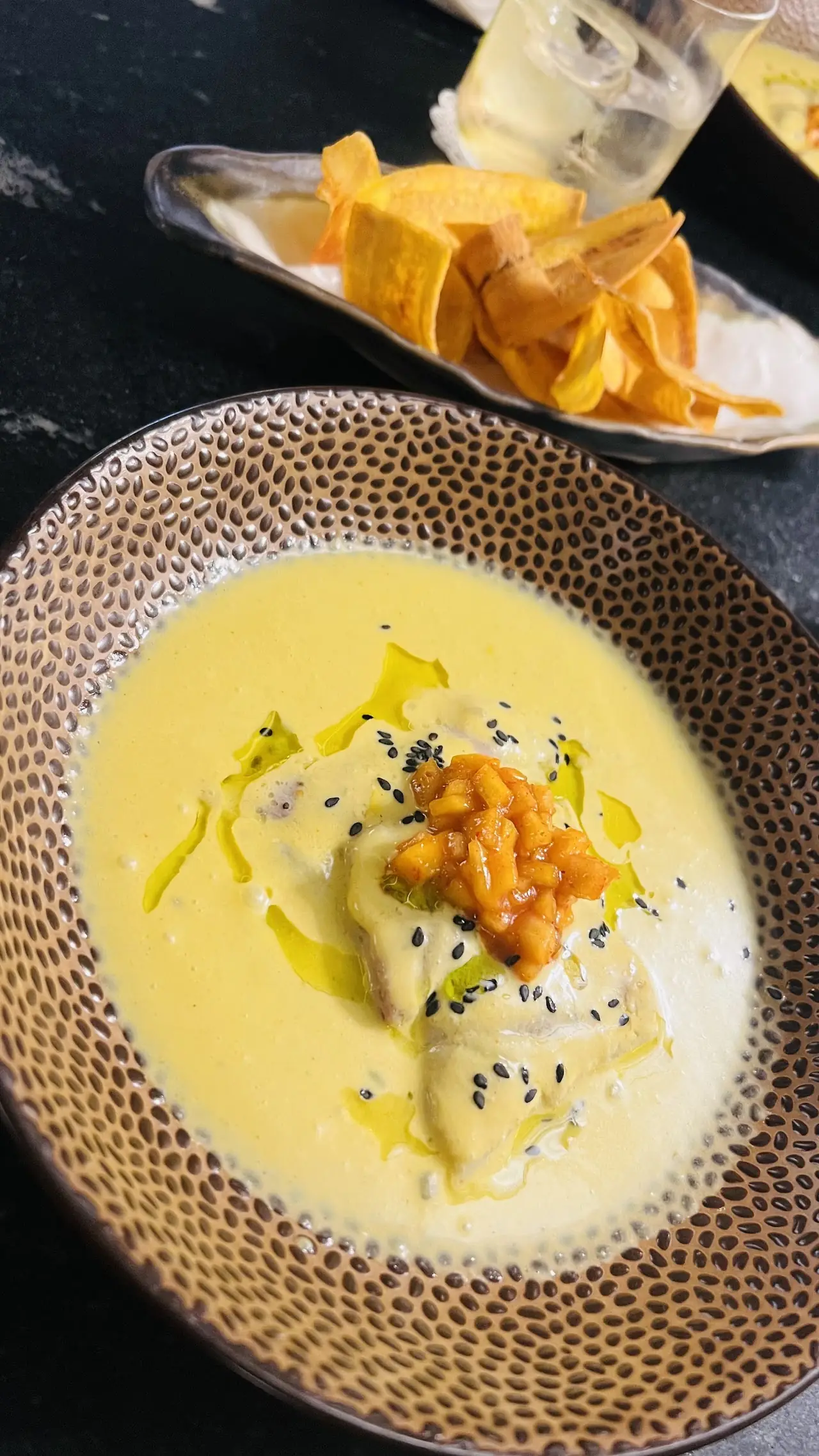 A yellow soup topped with black sesame seeds and an orange garnish