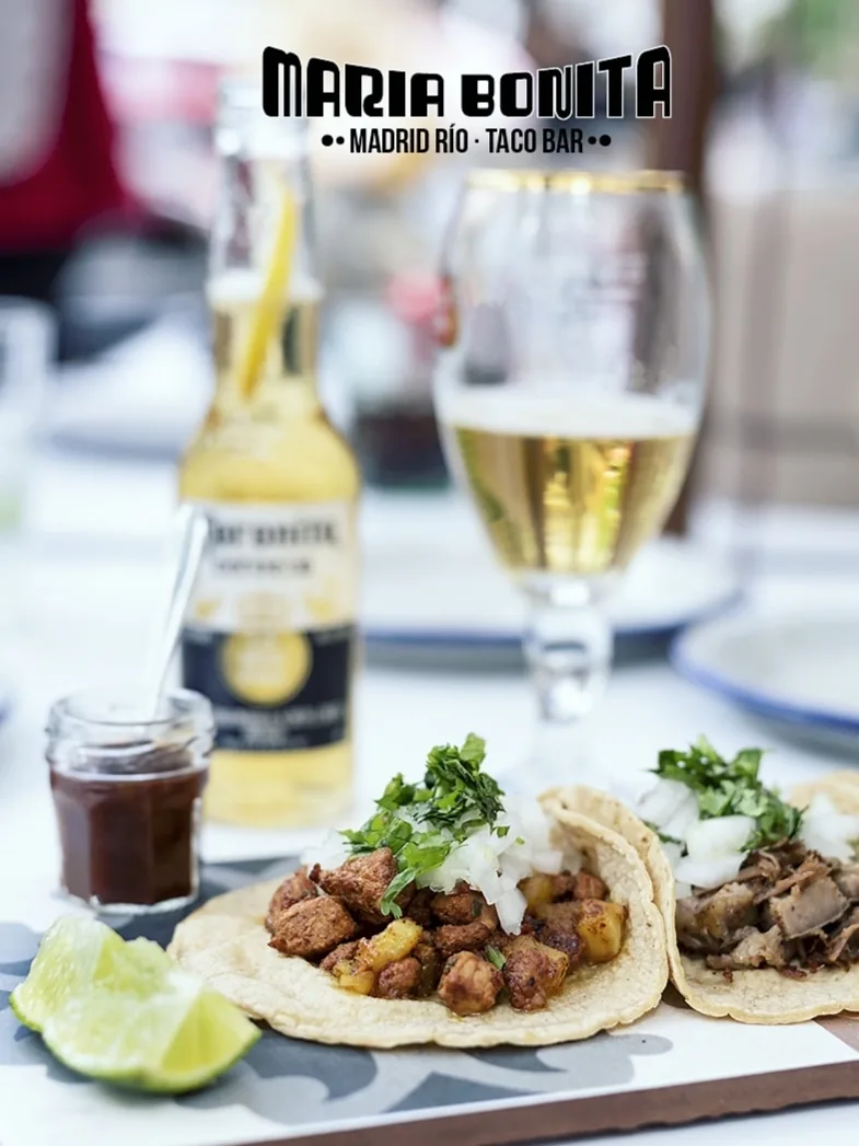 A soft taco with meat and cilantro beside a glass of beer