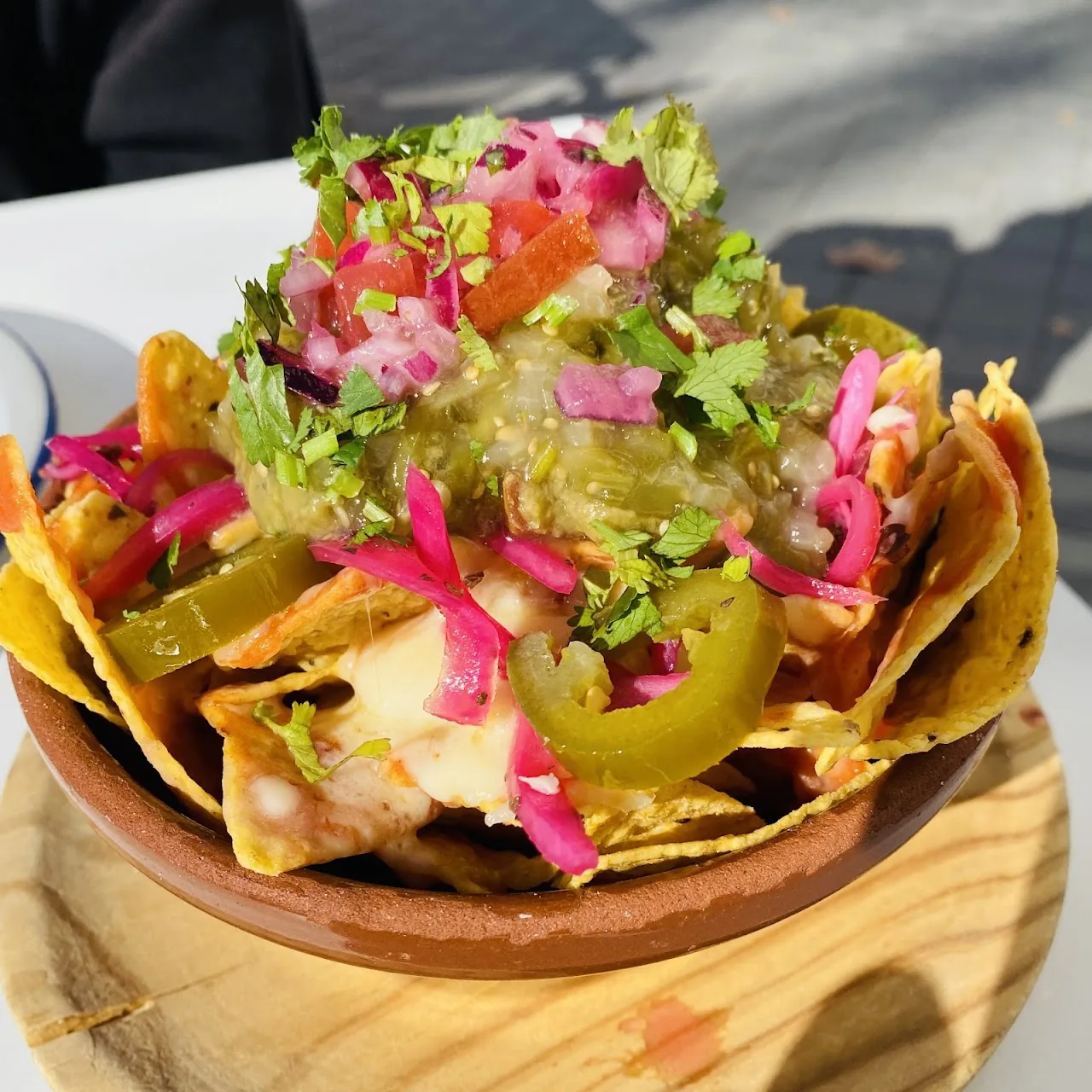 A tostada piled with nachos, pickled jalapeños and pink onion