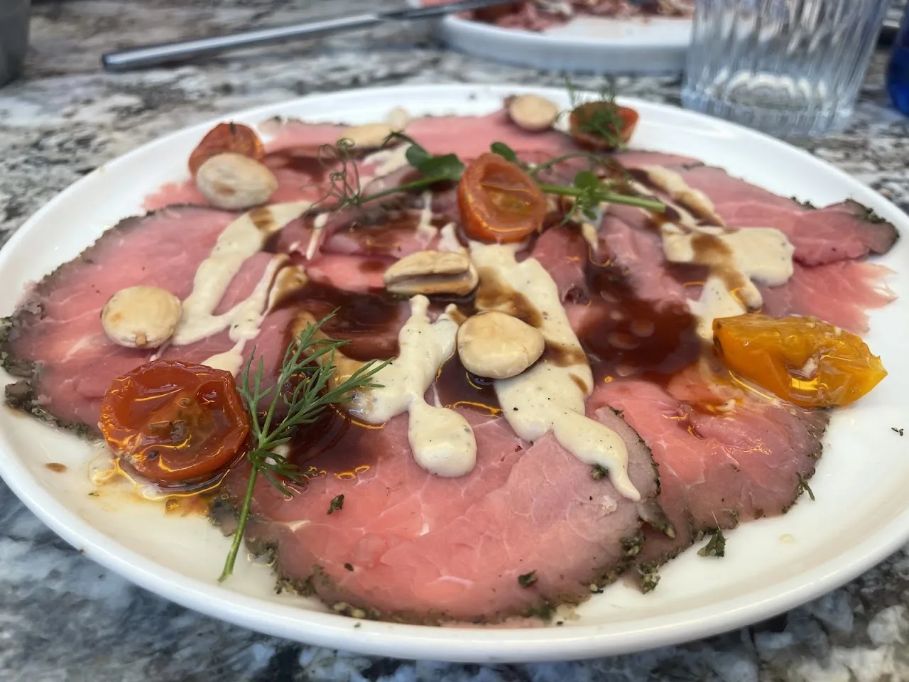 Sliced beef carpaccio with cherry tomatoes and a creamy sauce