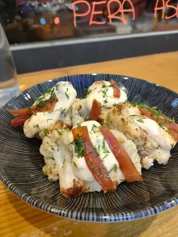 Roasted cauliflower florets in creamy sauce topped with strips of cured ham and dill in a blue-striped bowl
