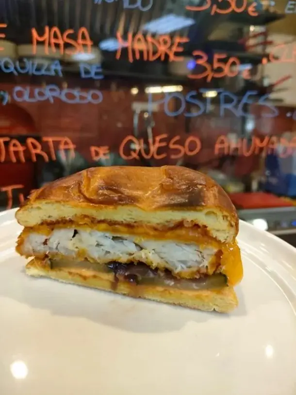 Cross-section of a fish burger with crispy white fish, melted cheese and pickle in a glossy brioche bun on a white plate