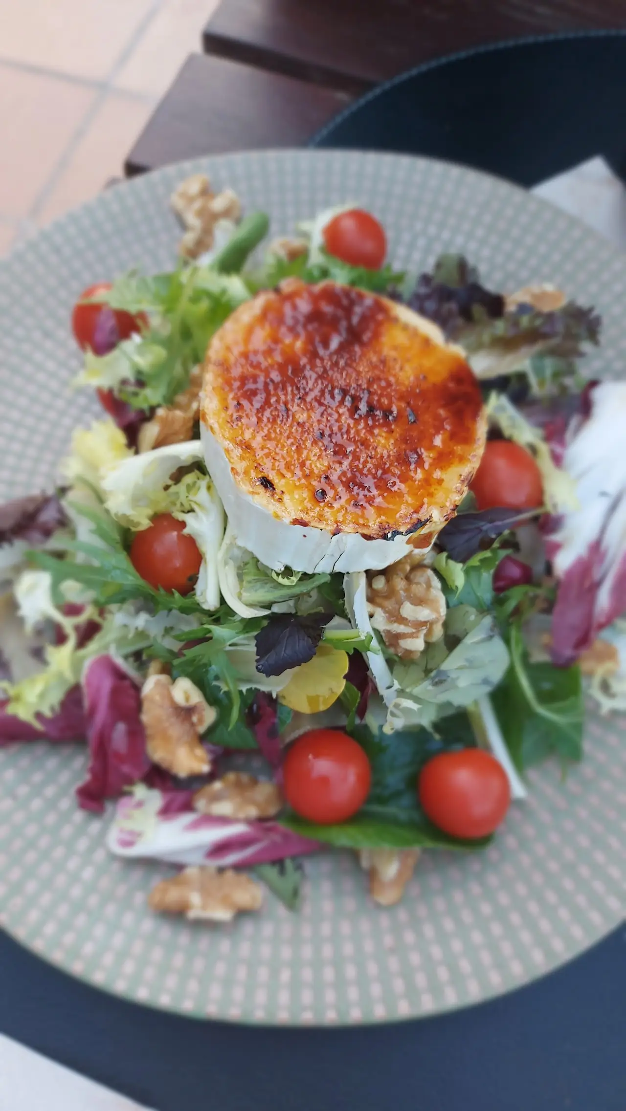 A warm goat cheese salad with walnuts and cherry tomatoes on a plate.