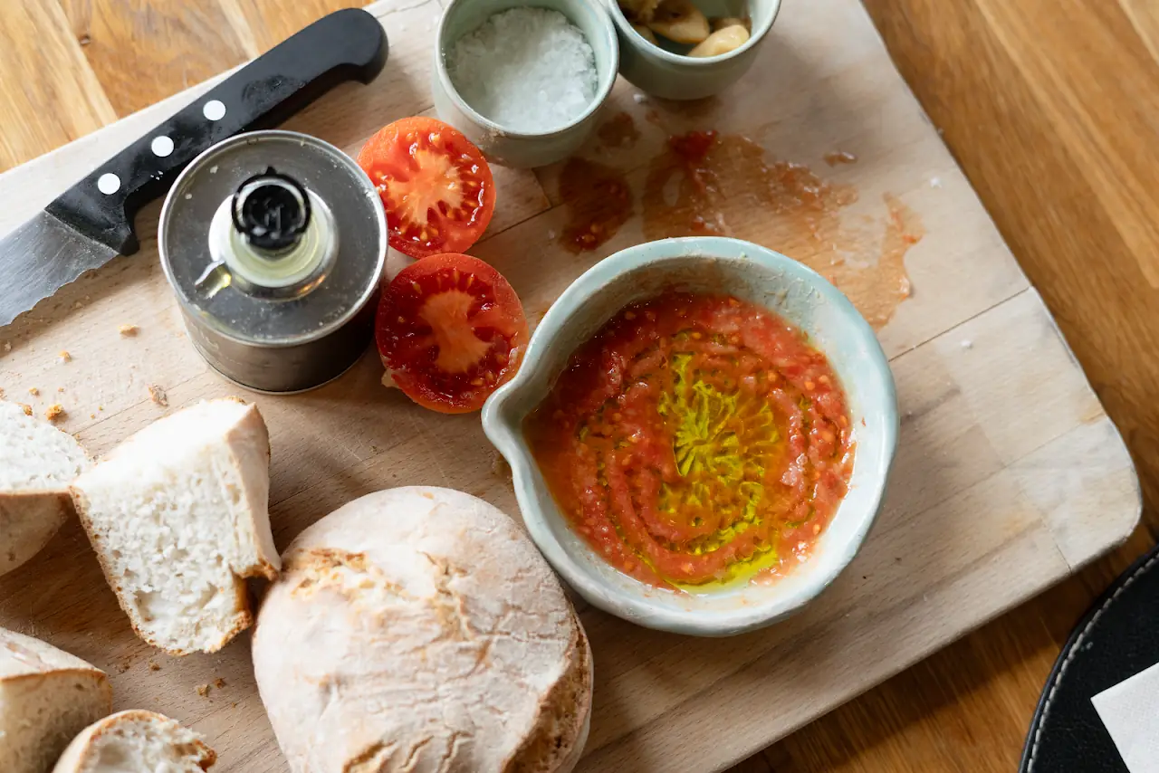 Toasted bread slices with a tomato spread, olive oil, and a pepper grinder on a wooden board.