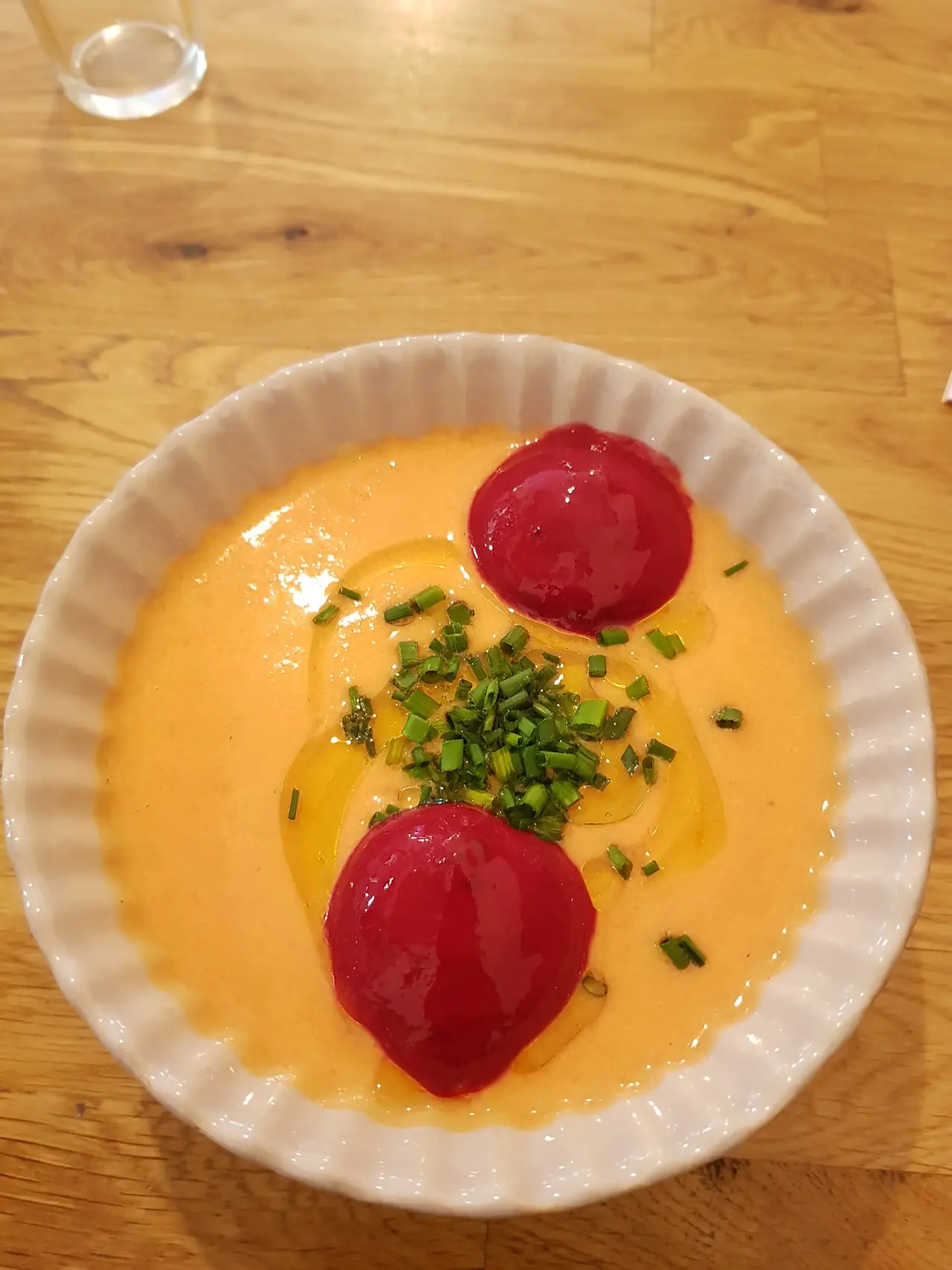 Chilled tomato soup topped with two red tomato-sorbet quenelles and chopped chives in a white bowl, at Market Cuina Fresca.