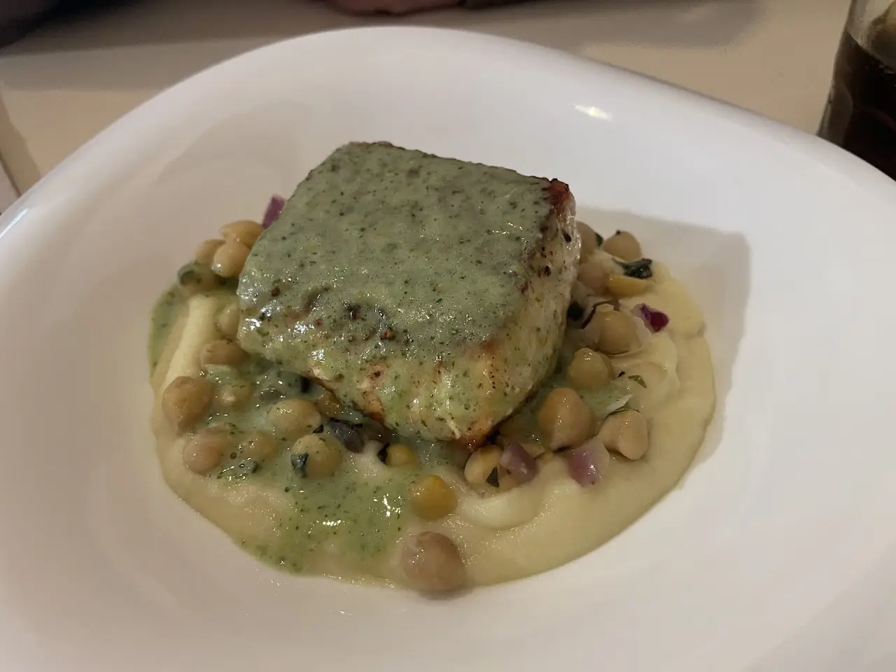 Herb-crusted fish over a chickpea and cream base on a white plate, at Market Cuina Fresca.