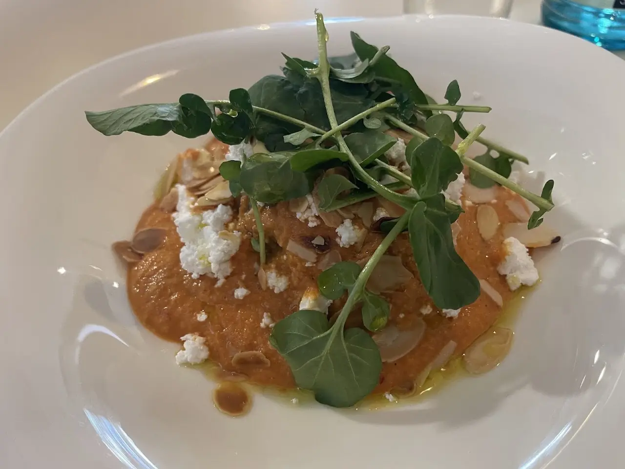 Plate with a romesco-style base, fresh goat cheese and dressed arugula, at Market Cuina Fresca.