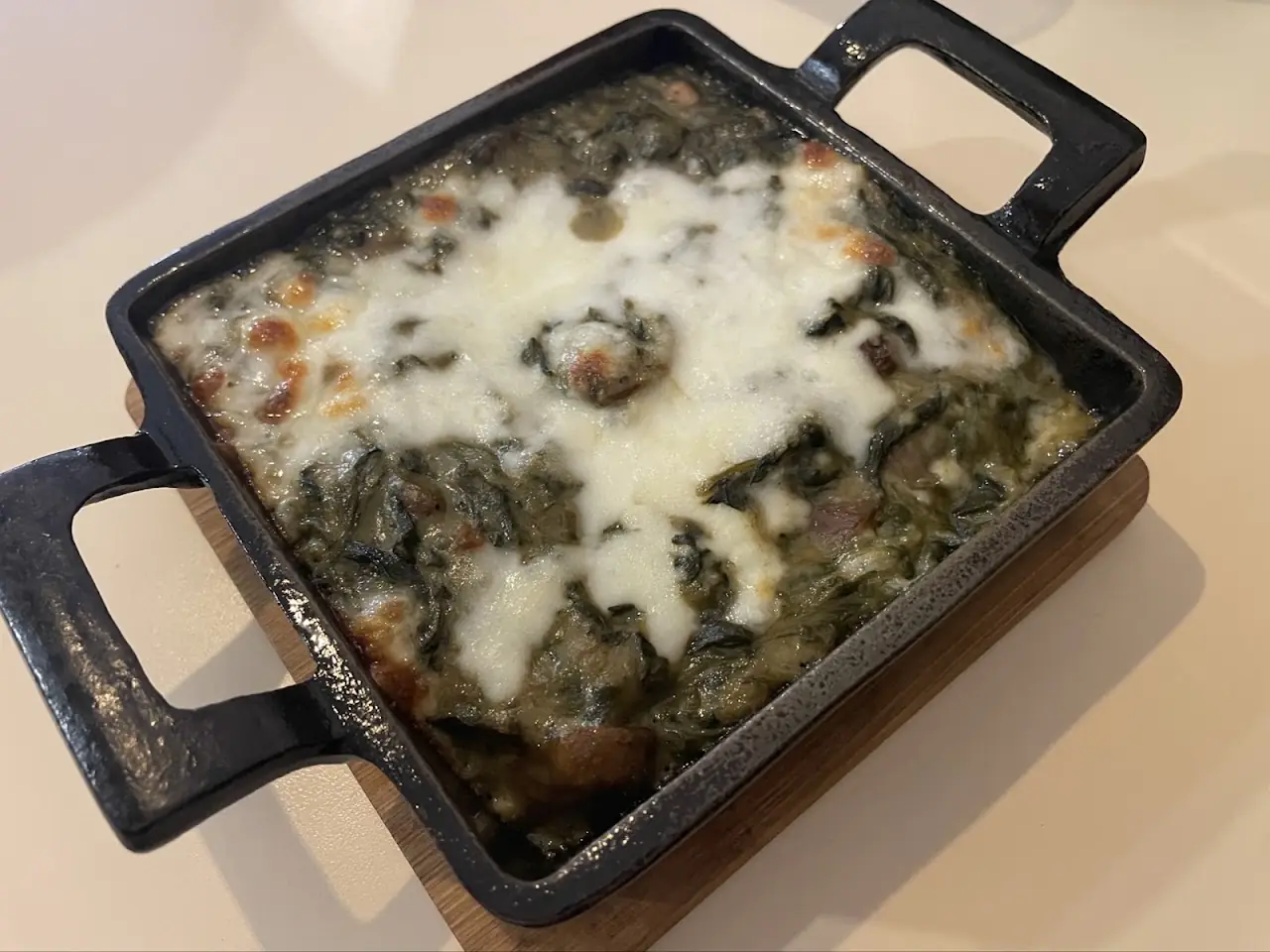 Baked greens gratin topped with melted cheese in a cast-iron dish, at Market Cuina Fresca.