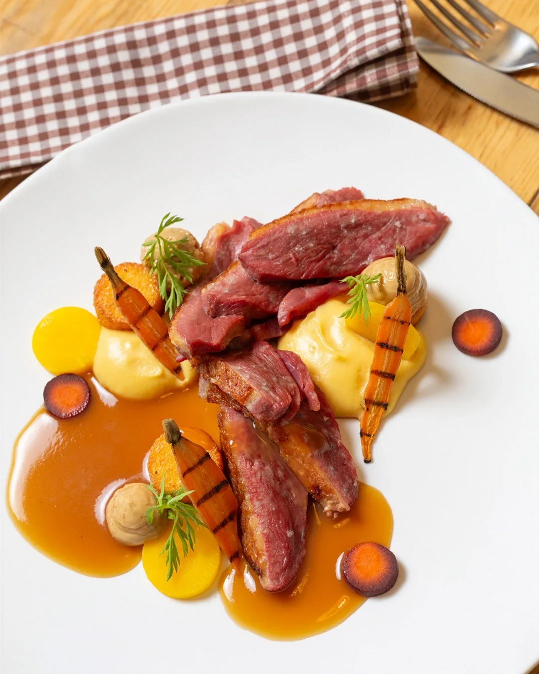 Slices of duck breast on a white plate with carrot, purée and an orange sauce