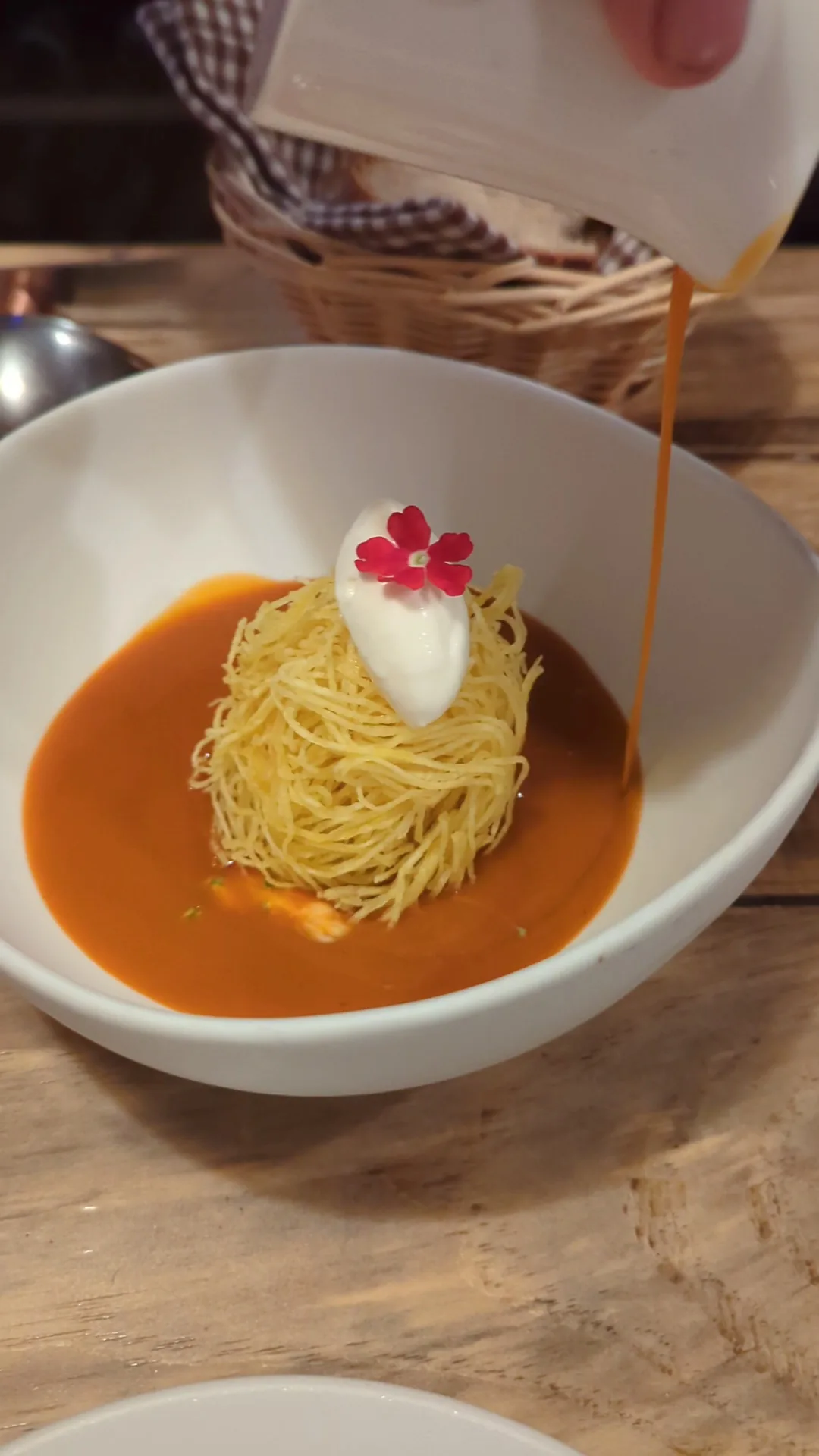 A bowl of thin noodles in a red broth with a delicate foam garnish