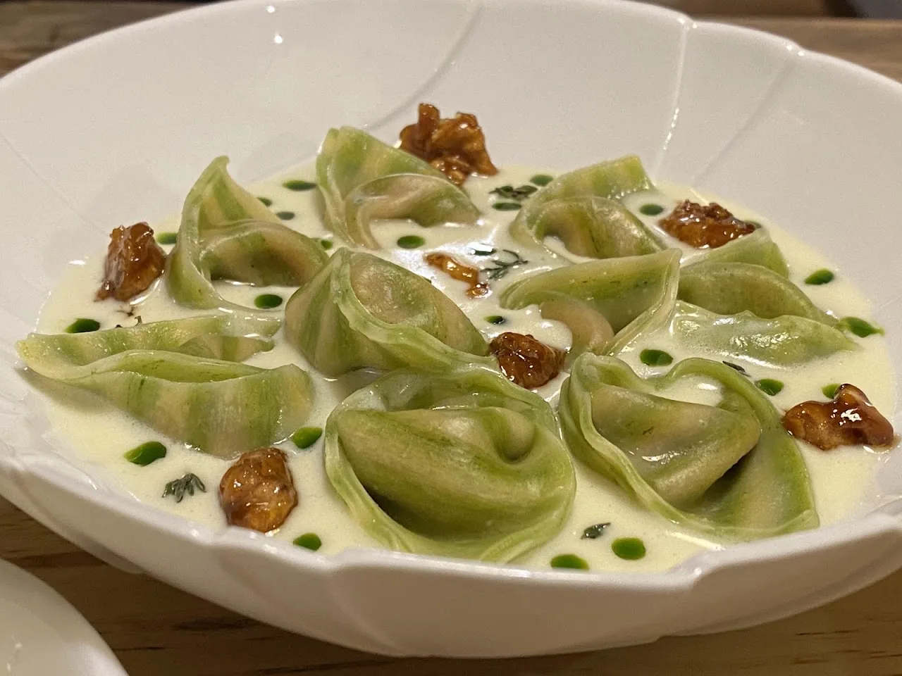 Green ravioli dumplings in a creamy sauce with crispy garnish