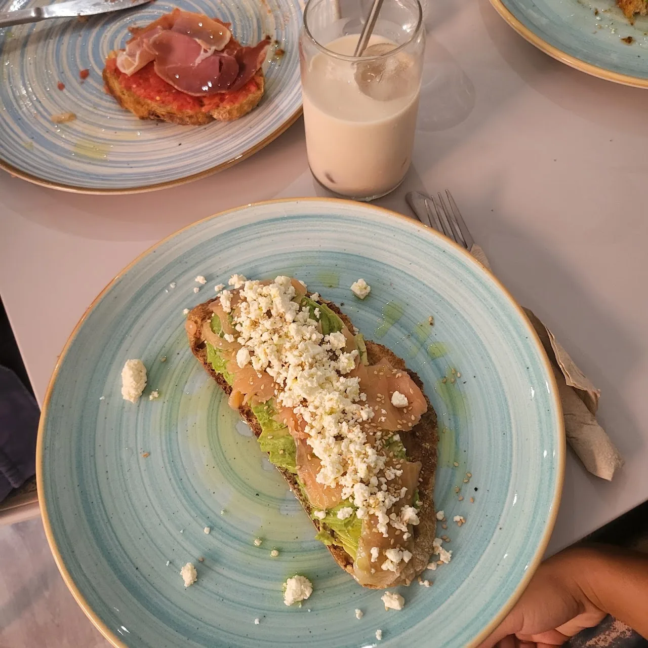 A slice of avocado toast beside a glass of iced coffee drink