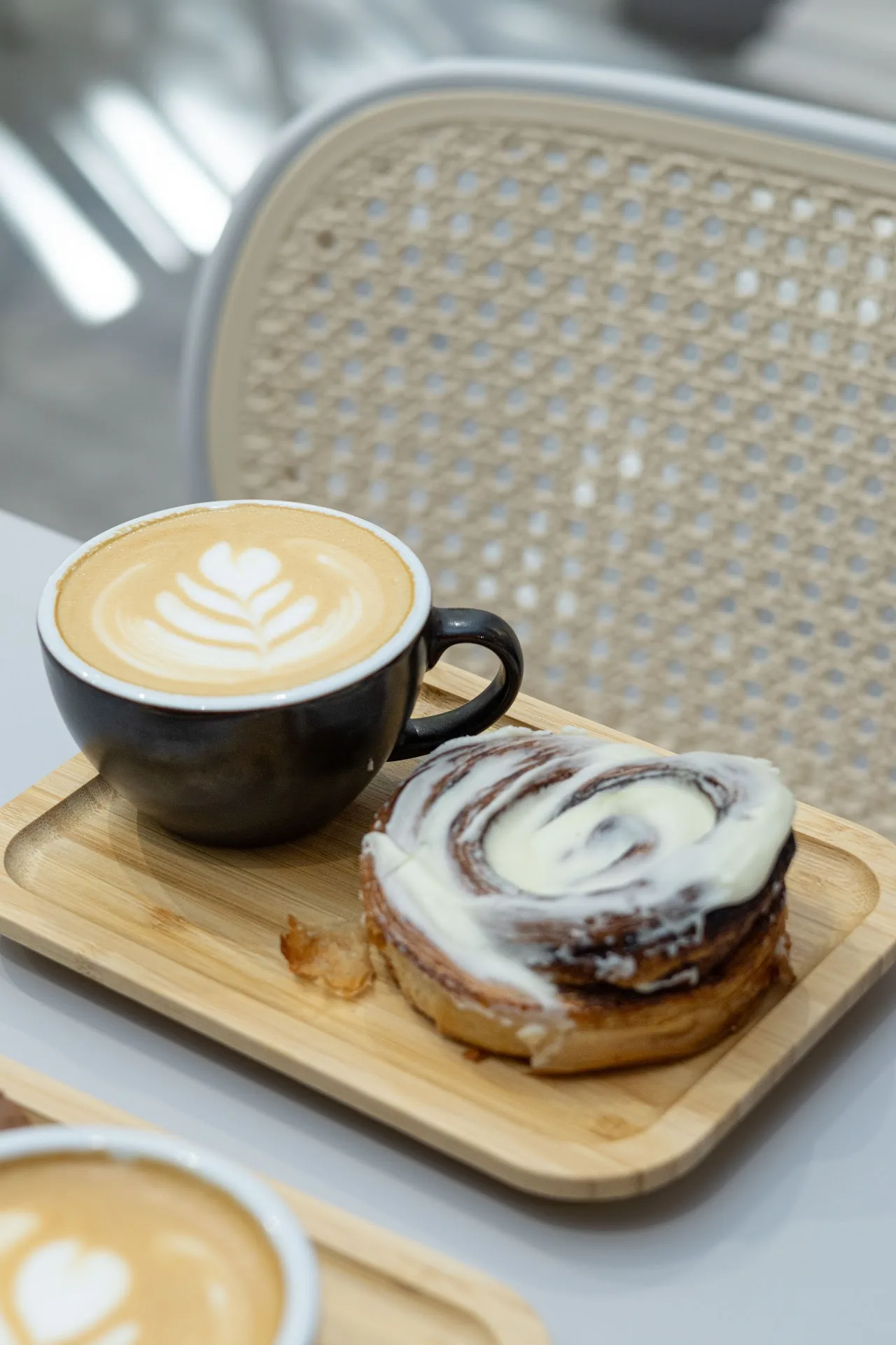 A latte with leaf latte art next to a swirled cinnamon roll on a wooden tray