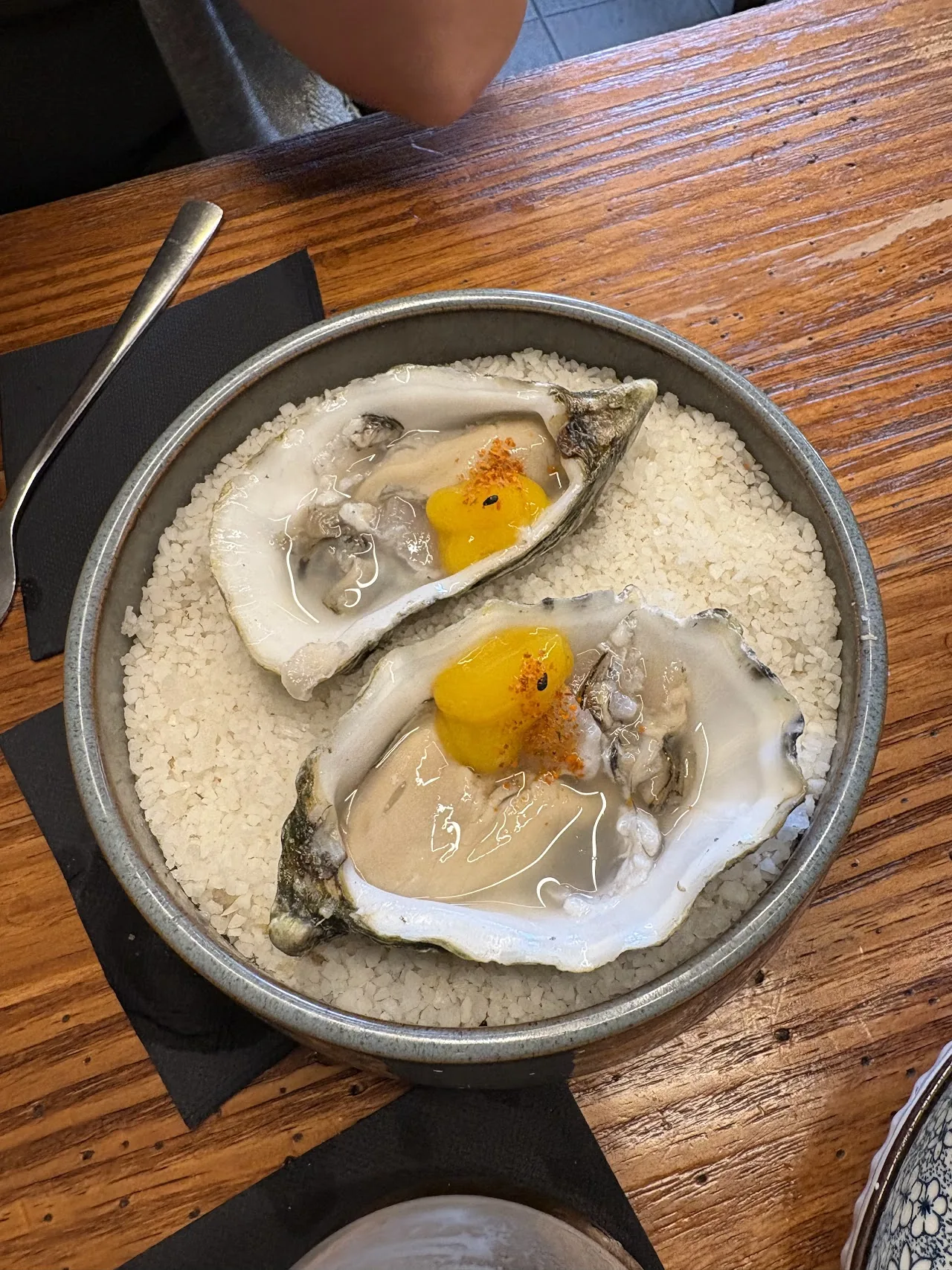 Two oysters on the half shell topped with a golden sauce and citrus