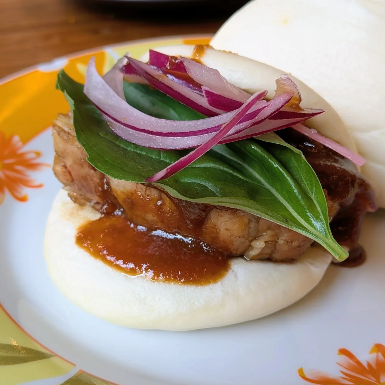A steamed bao bun filled with roast pork, pickled red onion, and greens